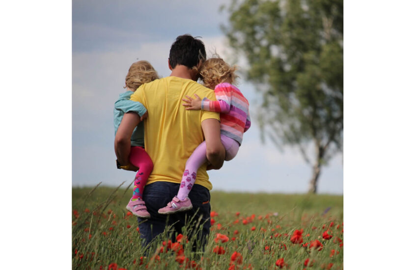 dad holding his two daughters in poppy field
